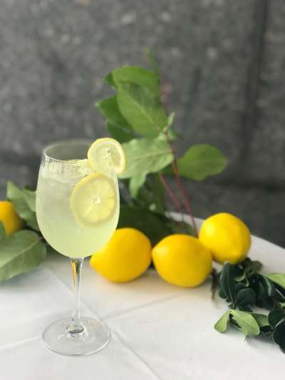 Limoncello spritz in a wine glass with a lemon round garnish, whole lemons and their greenery on the table in the background