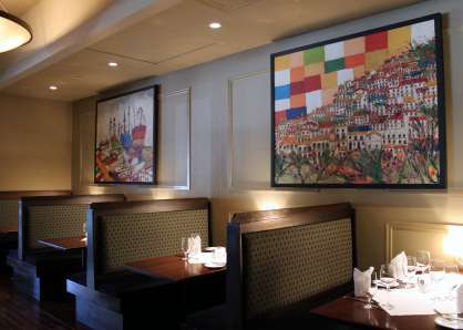Restaurant booths lit by soft candle light, beneath colorful photos of Mediterranean coastal villages and harbors