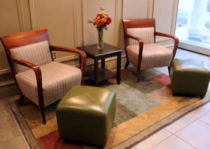 Two armchairs and green leather ottomans with an occasional table and floral arrangement in between, on a brightly patterned rug