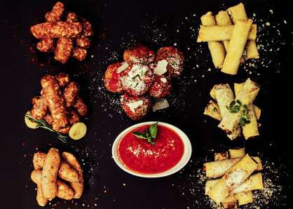 Sausages, spring rolls sprinkled with parmesan, and meatballs with marinara, all arranged on a black stone board