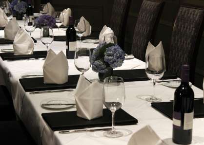 Closeup of long table set with menus, napkins folded into crown shapes, and blue hydrangea centerpieces