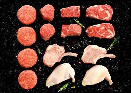 Raw steaks, burgers, pork chops, and chicken on a black stone background with springs of rosemary