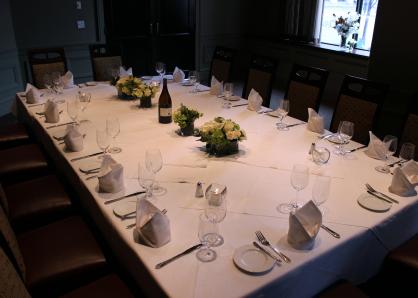 A room with glass-doored wine refrigerators in the walls and sheer curtains for privacy on one end. A long table is set for 16 and surrounded by high-backed chairs