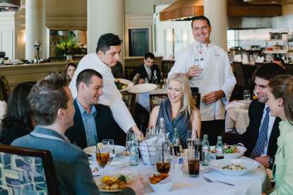 Five people enjoy dinner and drinks in the open Davio's Boston dining room, while servers pour water and bring additional dishes