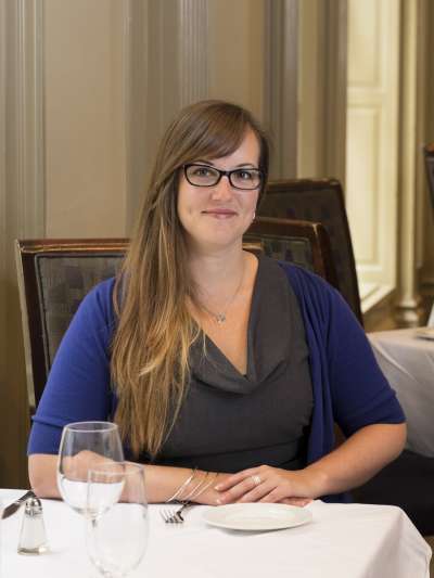 Beth Blakely, with glasses and long hair thrown over one shoulder, poses at a table in the Davio's dining room