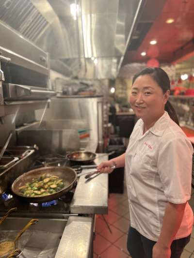 Woman in kitchen, sautéing vegetables, white chef coat