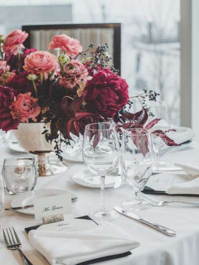 A numbered table with individual place cards and menu, a low centerpiece of a silver bowl of peonies and other flowers in various shades of pink