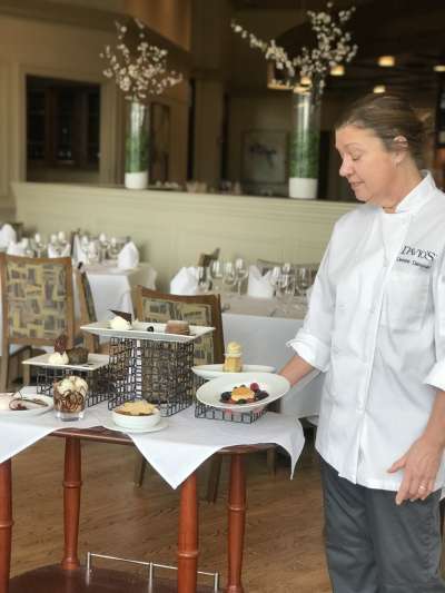 Denise Demoney, a Caucasian woman with brown hair pulled back, looks down as she arranges a display table of desserts