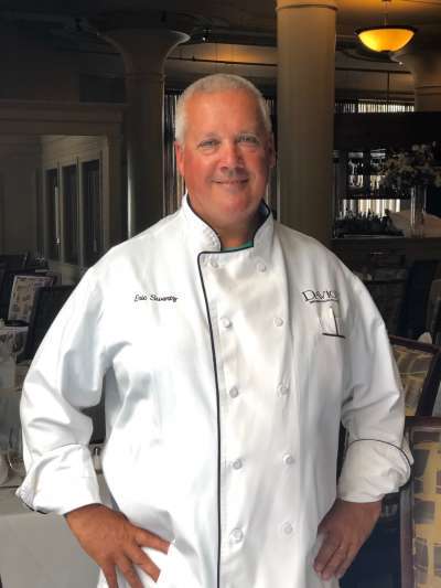 Eric Swartz, a Caucasian man with close-cropped gray hair, poses in chefs whites with hands on hips in the Davio's dining room