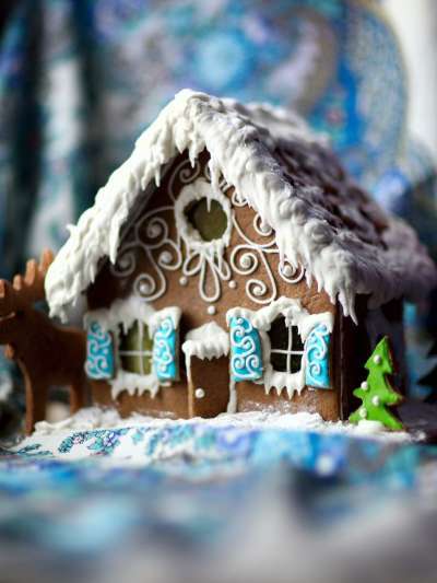 A gingerbread house decorated with snow-frosting on the roof, ice sickles hanging from the door and windows, and robins egg blue shutters on the windows.