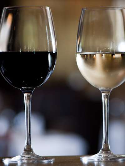 A glass of red wine and a glass of white wine sit side by side on a table with the background in soft focus