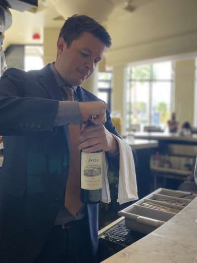 Man, Blue suit, orange tie, short dark hair, opening bottle of wine