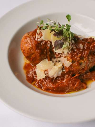 Meatballs in chunky tomato sauce with shaved parmesan cheese and garnished with microgreens