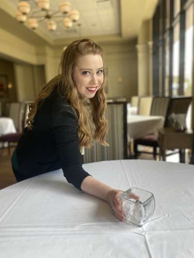 Woman, Long Curly Blonde Hair, Green Shirt, Placing a candle on table