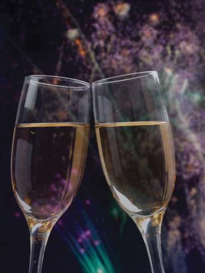 Two flutes of champagne clink in front of a dark sky bursting with fireworks