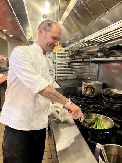 Man chef coat cooking asparagus in kitchen