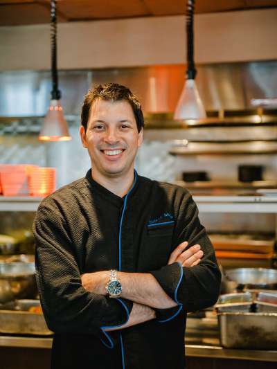 Rodney Murillo stands, smiling with arms folded, wearing black chefs' clothing, in Davio's kitchen