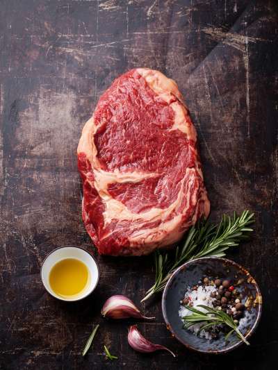 Raw Ribeye Steak, side olive oil, kosher salt, peppercorns, leaf