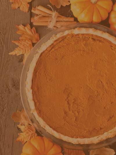 Top view of a pumpkin pie on a wooden table, surrounded by miniature pumpkins, fall leaves, and a bundle of cinnamon sticks