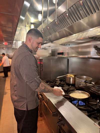 Man, short hair, grey Chef Jacket sautéing in the kitchen