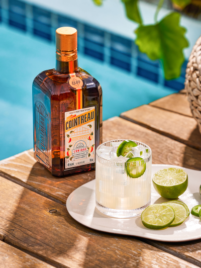 Bottle of Cointreau with limes on a table, pool in the background