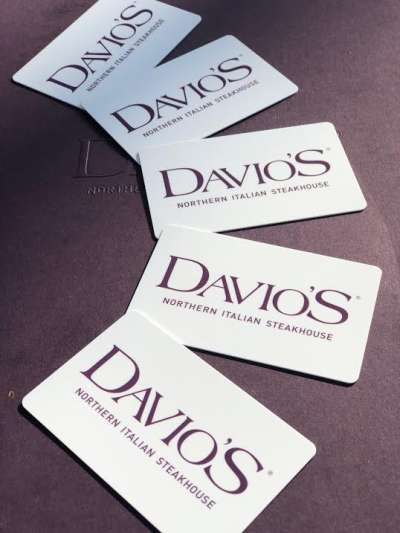 Five white plastic gift cards featuring the Davio's logo in purple, fanned out on a dark background