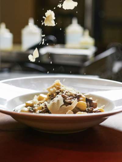 White dish of gnocchi, mushrooms, cheese and cheese falling thru air