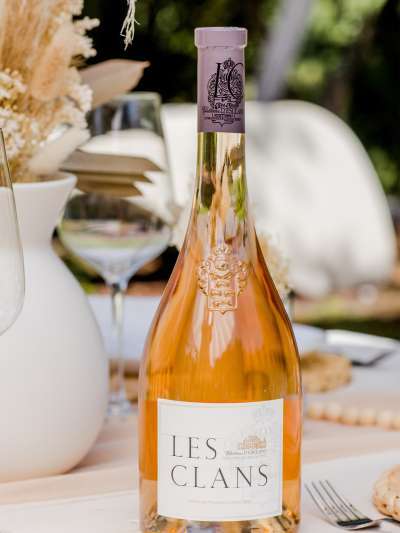 Bottle of Les Clans Wine on a table with a glass and flowers in a vase