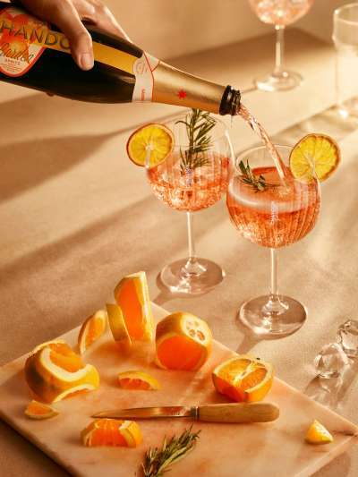 Pouring Chandon Rose into glasses with orange wheel and cut oranges on a cutting board