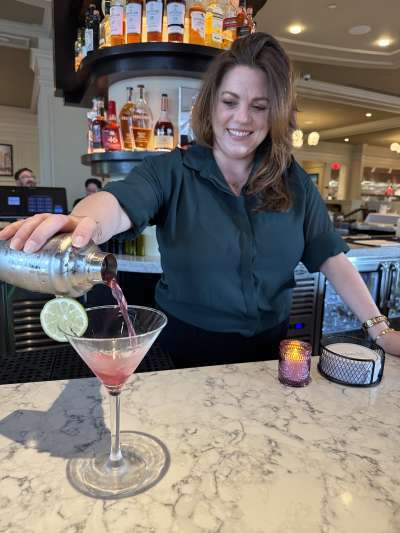 Woman standing behind the bar pouring a martini
