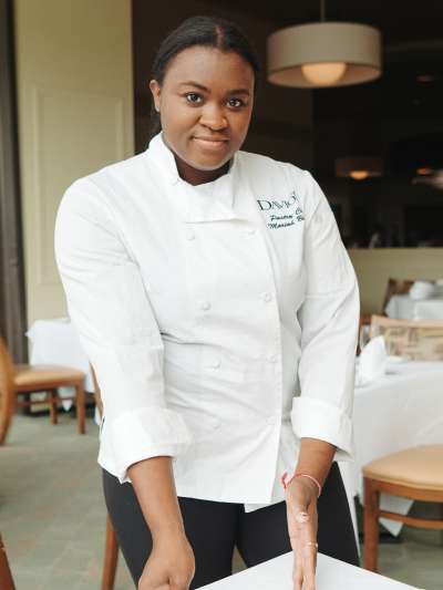 Woman, White Chef Coat, Dark Hair, Holding Plate of Chocolate Cake