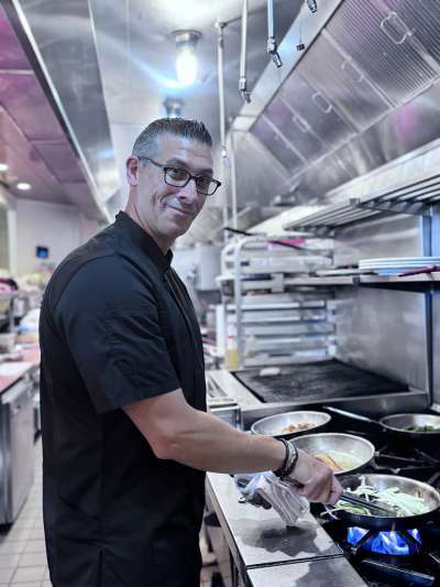 Man Black Chef Jacket sautéing over an oven