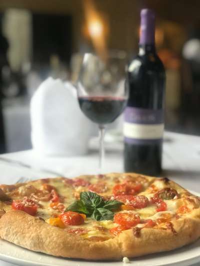Pizza with basil and cherry tomatoes, a glass of red wine, and a Davio's-labeled wine bottle