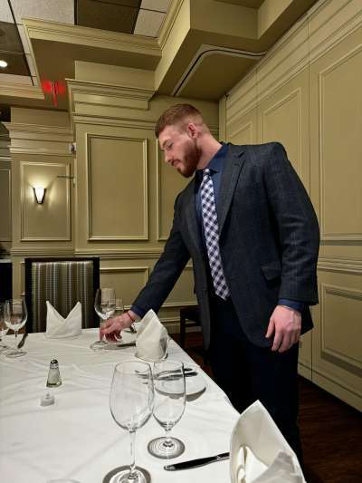 Man dark suit, beard, red hair setting a table