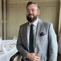 Man gray suit, beard, leaning on a chair