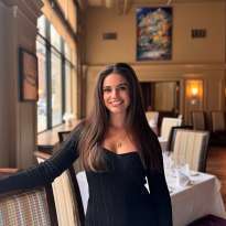 Woman, long dark hair, black dress leaning on a chair