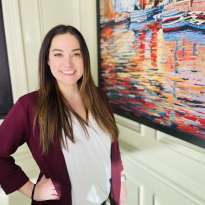 Woman Long dark hair, purple sweater, white shirt next to a painting