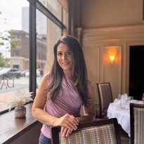 Woman long dark hair, leaning on a chair, pink shirt, purple pants
