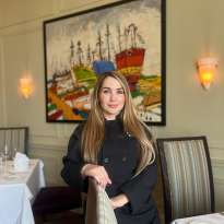 Woman, Long Hair, Black Chef Coat, Leaning on a chair in front of a Madrid painting