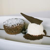 An individual-sized warm chocolate cake, disted with powdered sugar, sits next to a scoop of vanilla bean ice cream topped with a triangular piece of dark chocolate.