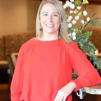 Woman, Blond hair, Red shirt, Black Pants leaning on the bar