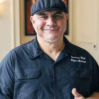 Man, Black Chef Jacket, Dark Hat, Holding a plate of Sliced Steak