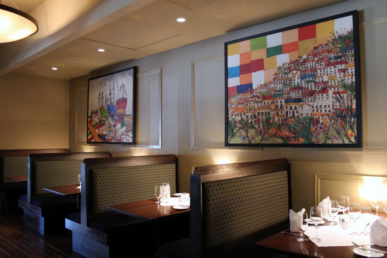Restaurant booths lit by soft candle light, beneath colorful photos of Mediterranean coastal villages and harbors