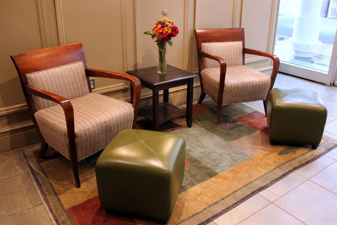 Two armchairs and green leather ottomans with an occasional table and floral arrangement in between, on a brightly patterned rug