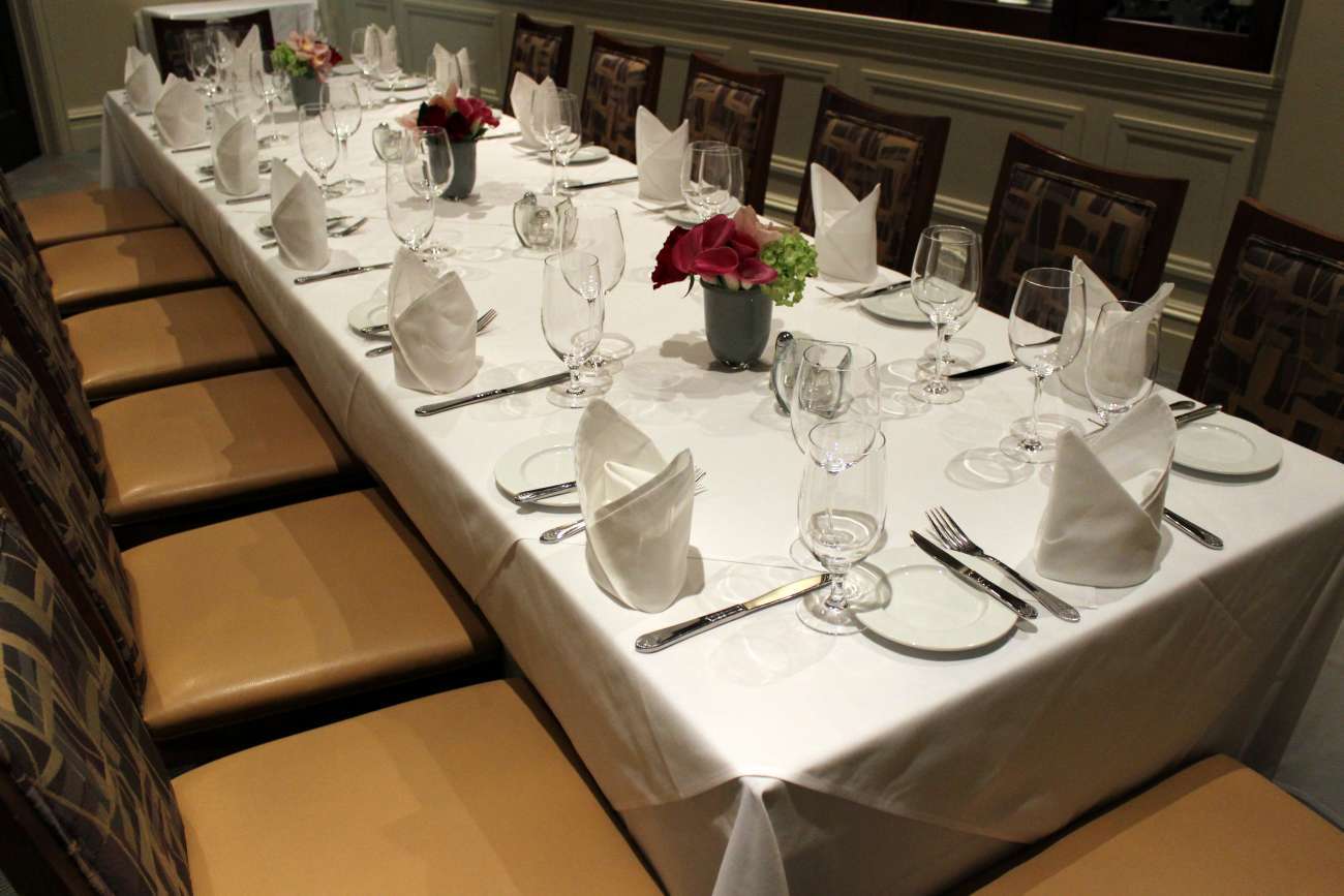 Closeup of a long, 20-person table, with full place settings, cloth napkins, and flowers in the Wine Room and 