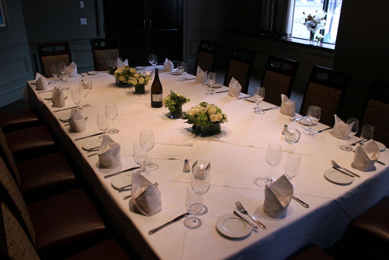 A room with glass-doored wine refrigerators in the walls and sheer curtains for privacy on one end. A long table is set for 16 and surrounded by high-backed chairs