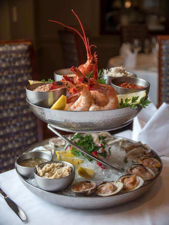 A two-tiered raw bar selection with oysters on the half shell, shrimp cocktail, Maine lobster, lump crab, clams, tuna, scallop crudo