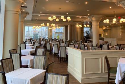 The main dining room features high ceilings, majestic columns with period cornice moldings, large wall-to-wall windows overlooking Boston Harbor with beautiful views of the ocean, warm wood tones with inviting wall colors.