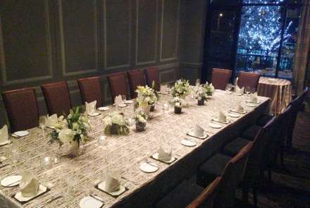 The Washington Room with a long table set for 16. Through the window, the trees outside are lit for the holidays.