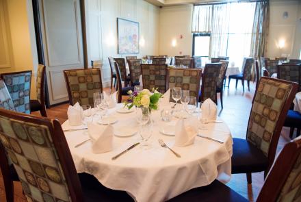 White tablecloths, flowers, round tables set for 6, and a sunny window in the combined Newbury/Walnut room.